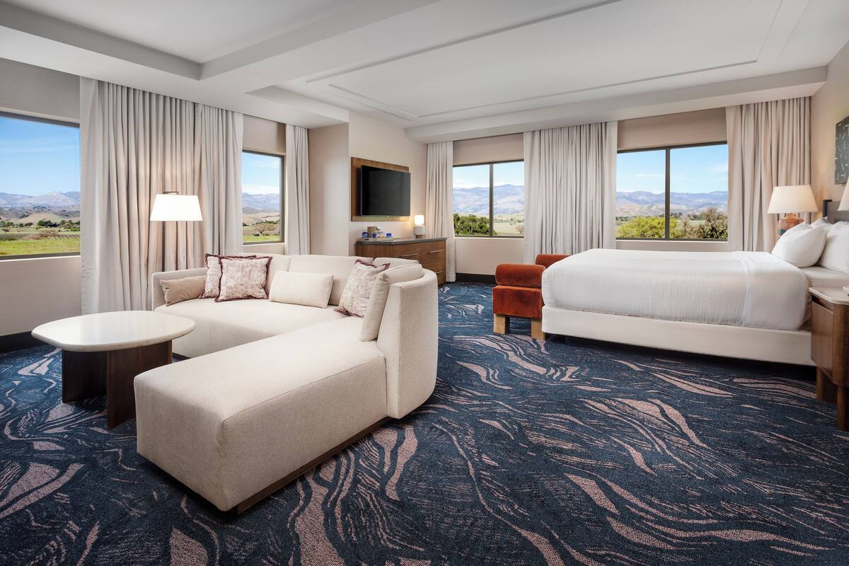 A hotel room with a large bed, a sofa, a small table, and a TV.
