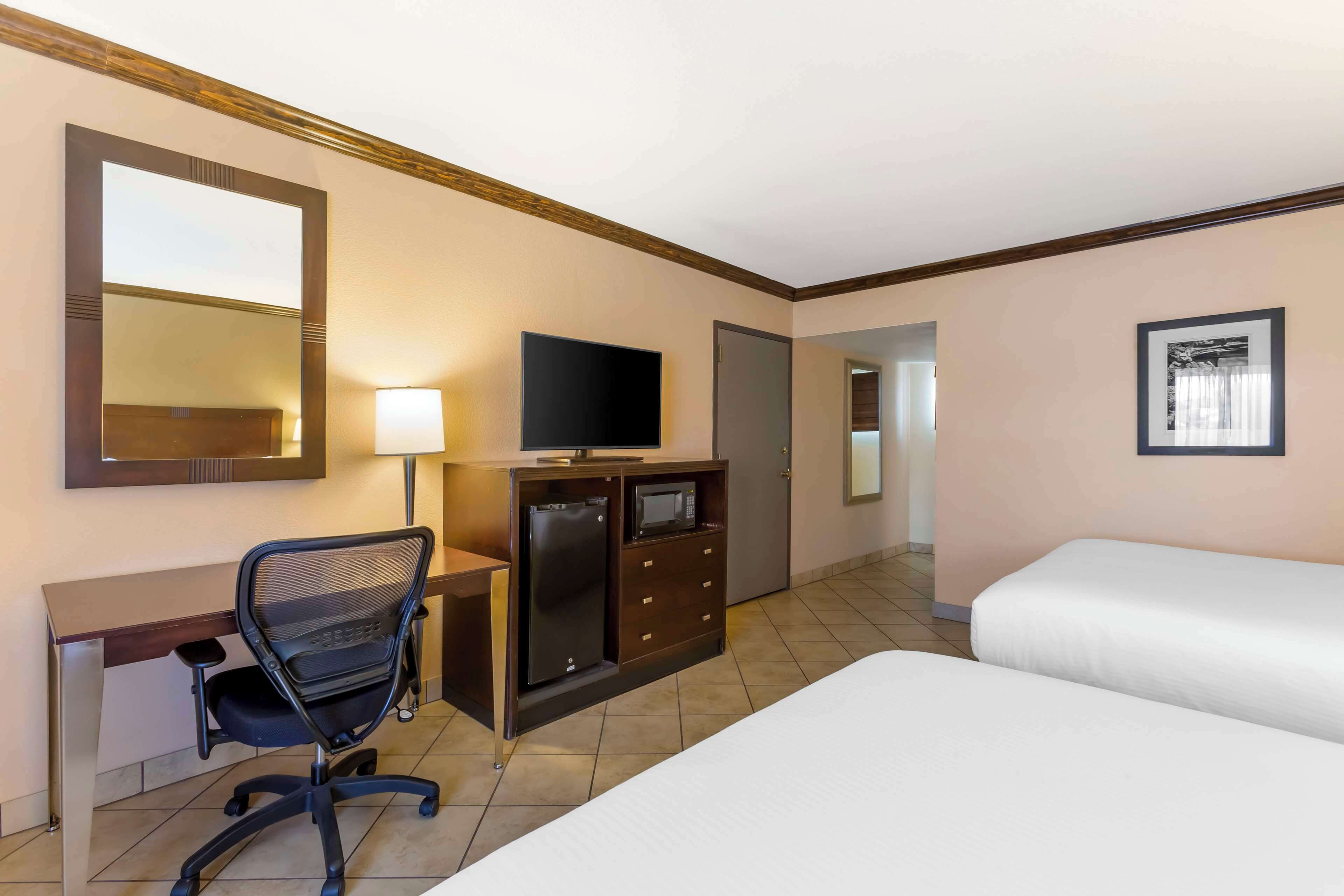 A hotel room with a desk, a chair, a television, a minibar, and two beds.