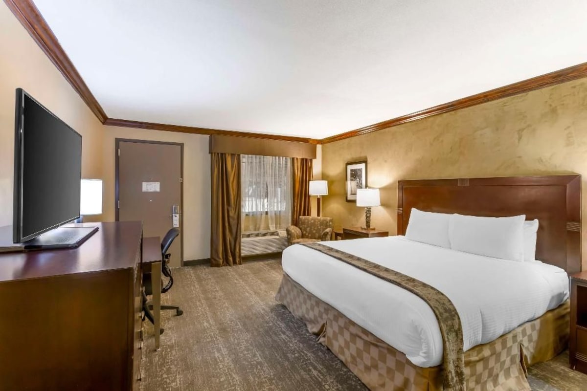 A hotel room with a bed, desk, television, and a door.