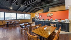 A restaurant with wooden tables and chairs, a kitchen counter with various dishes, and large windows offering a view of the outdoors. - Best Western Plus Raton Hotel (Raton)
