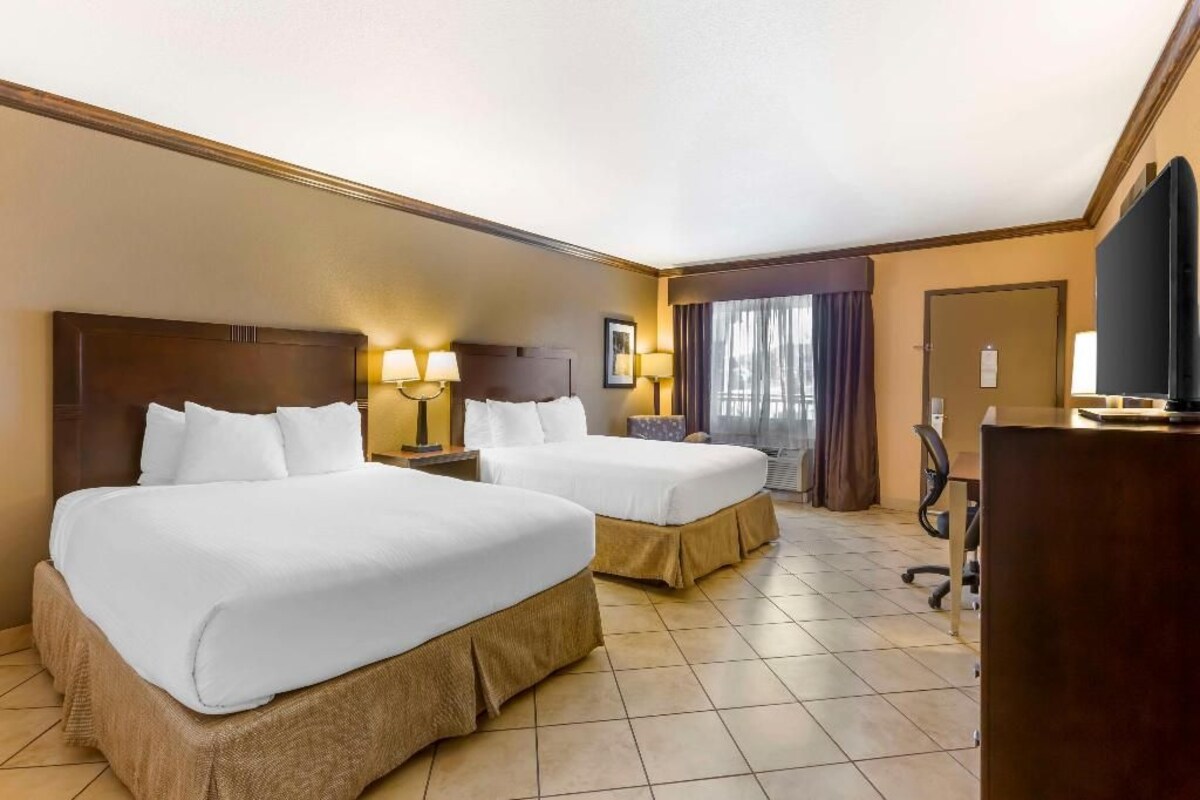 A hotel room with two beds, a desk, a chair, and a television.