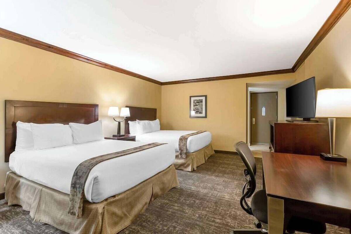 A hotel room with two beds, a desk, a television, and a framed picture on the wall.