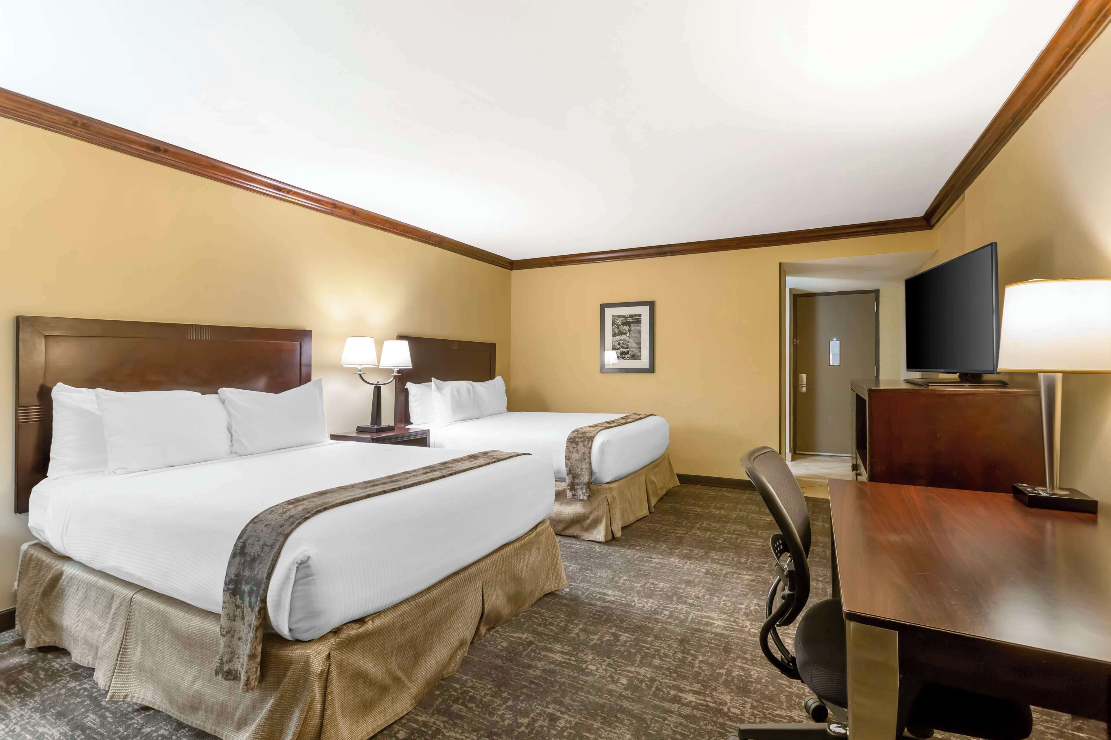 A hotel room with two beds, a desk, a television, and a framed picture on the wall.