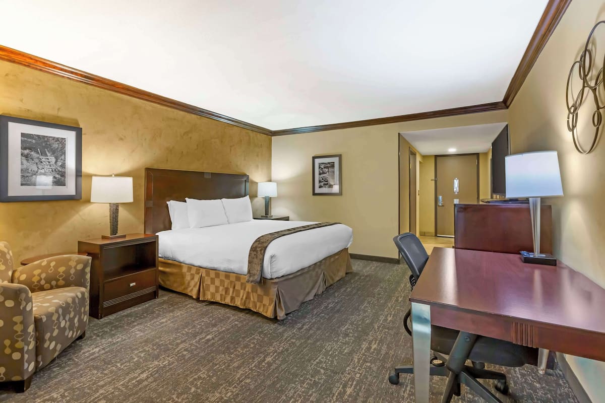 A hotel room with a bed, a desk, a chair, a nightstand, and two wall-mounted lamps.