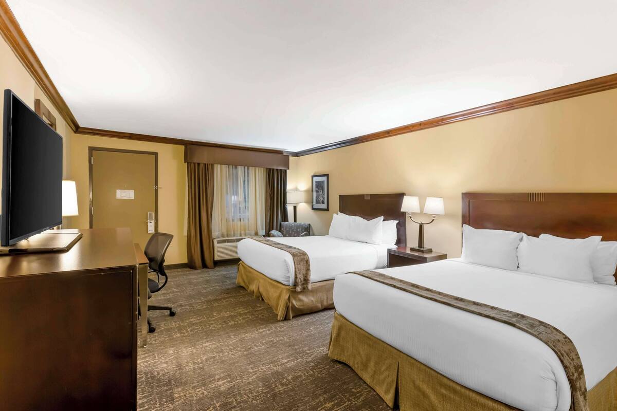 A hotel room with two beds, a desk, a chair, and a television.