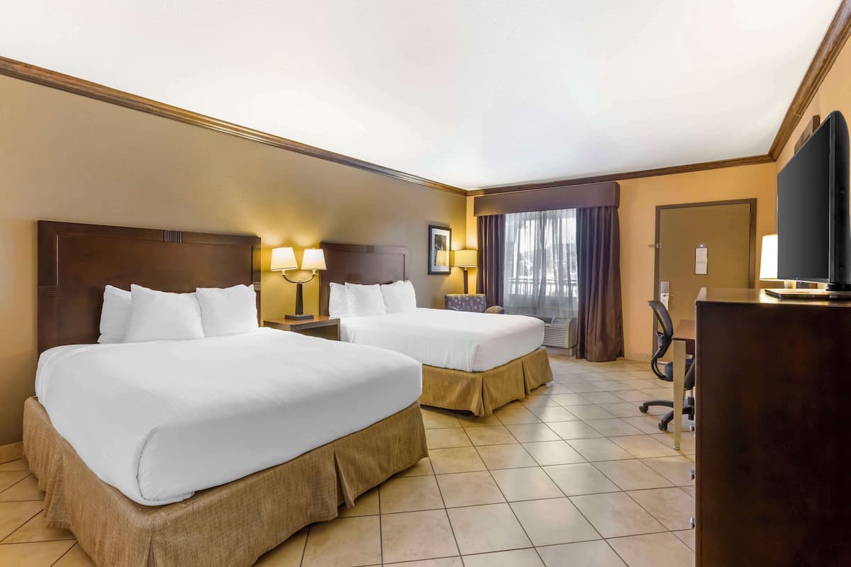 A hotel room with two beds, a desk, a television, and a window with curtains.
