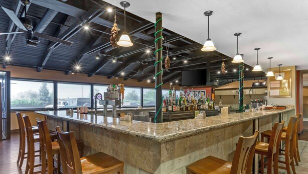 A bar area with a high ceiling, pendant lighting, and a bar counter with stools. - Best Western Plus Raton Hotel (Raton)