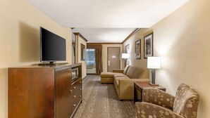 A compact hotel room with a television, a sofa, a small table with a lamp, and a cabinet. - Best Western Plus Raton Hotel (Raton)