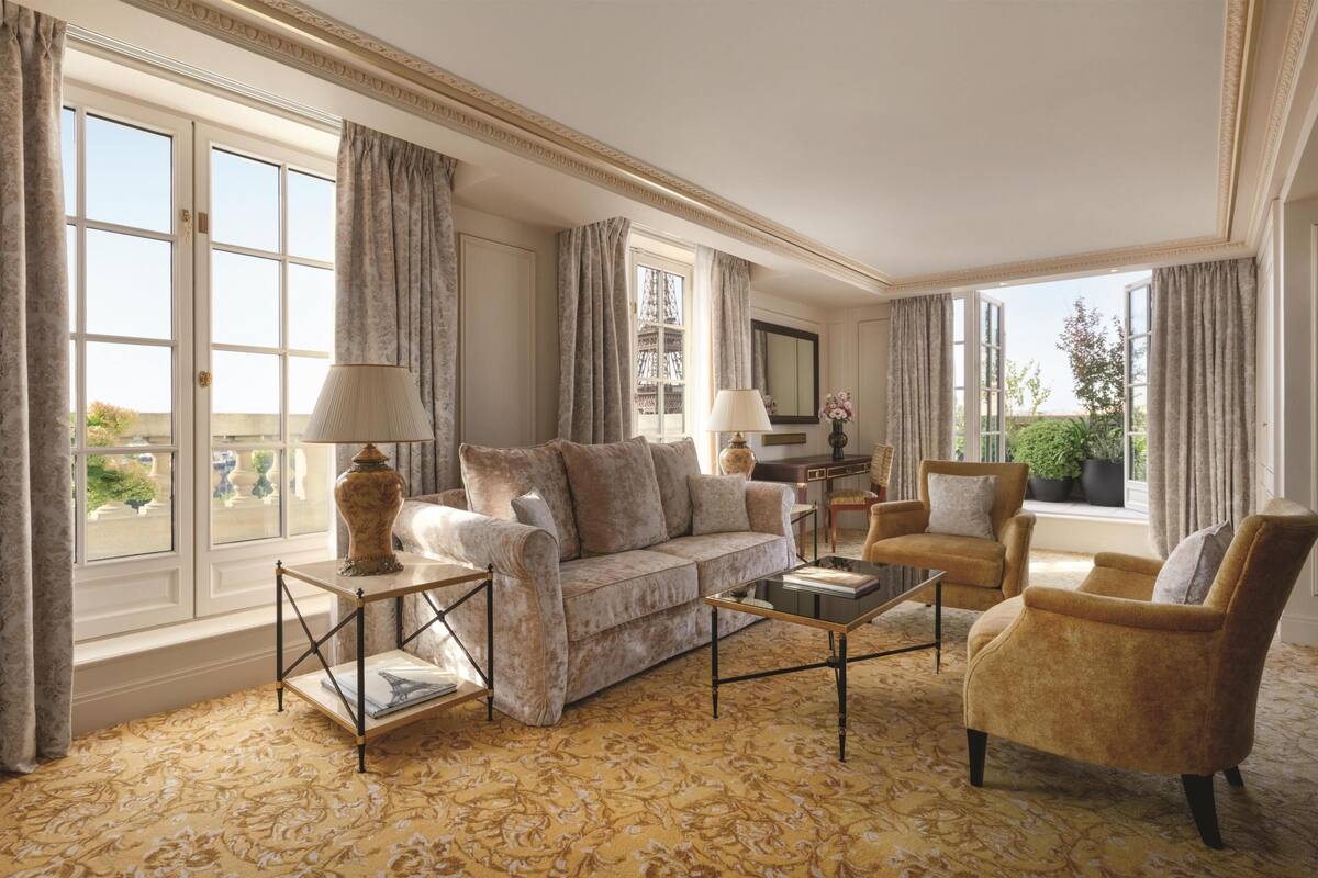 Un salon spacieux comprenant un canapé, des fauteuils, une table basse et une grande fenêtre avec des rideaux.