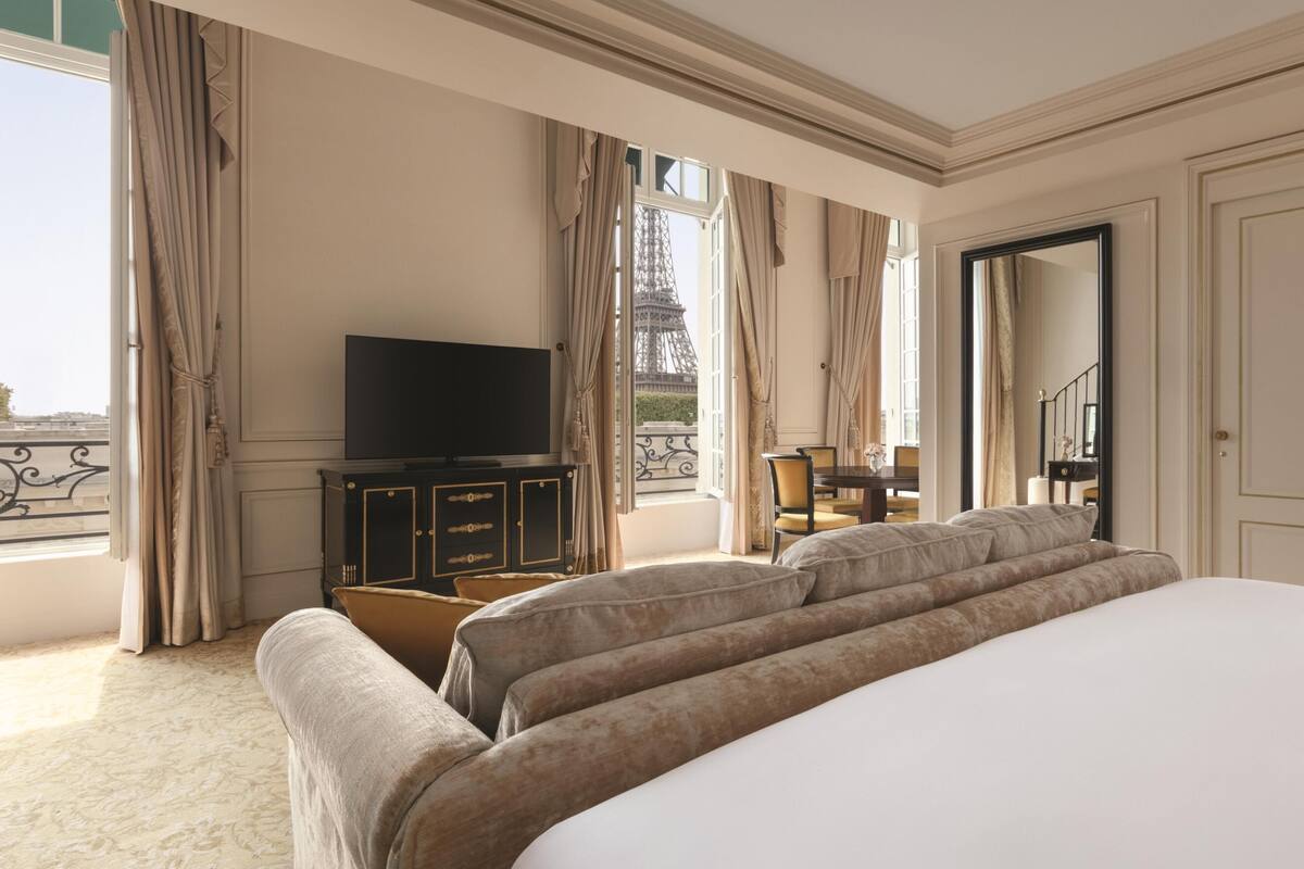 Une chambre d’hôtel avec un grand lit, une télévision, un bureau et une vue sur la Tour Eiffel.