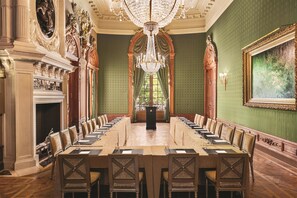A formal meeting room with a long table, chairs, a chandelier, and ornate decorations.