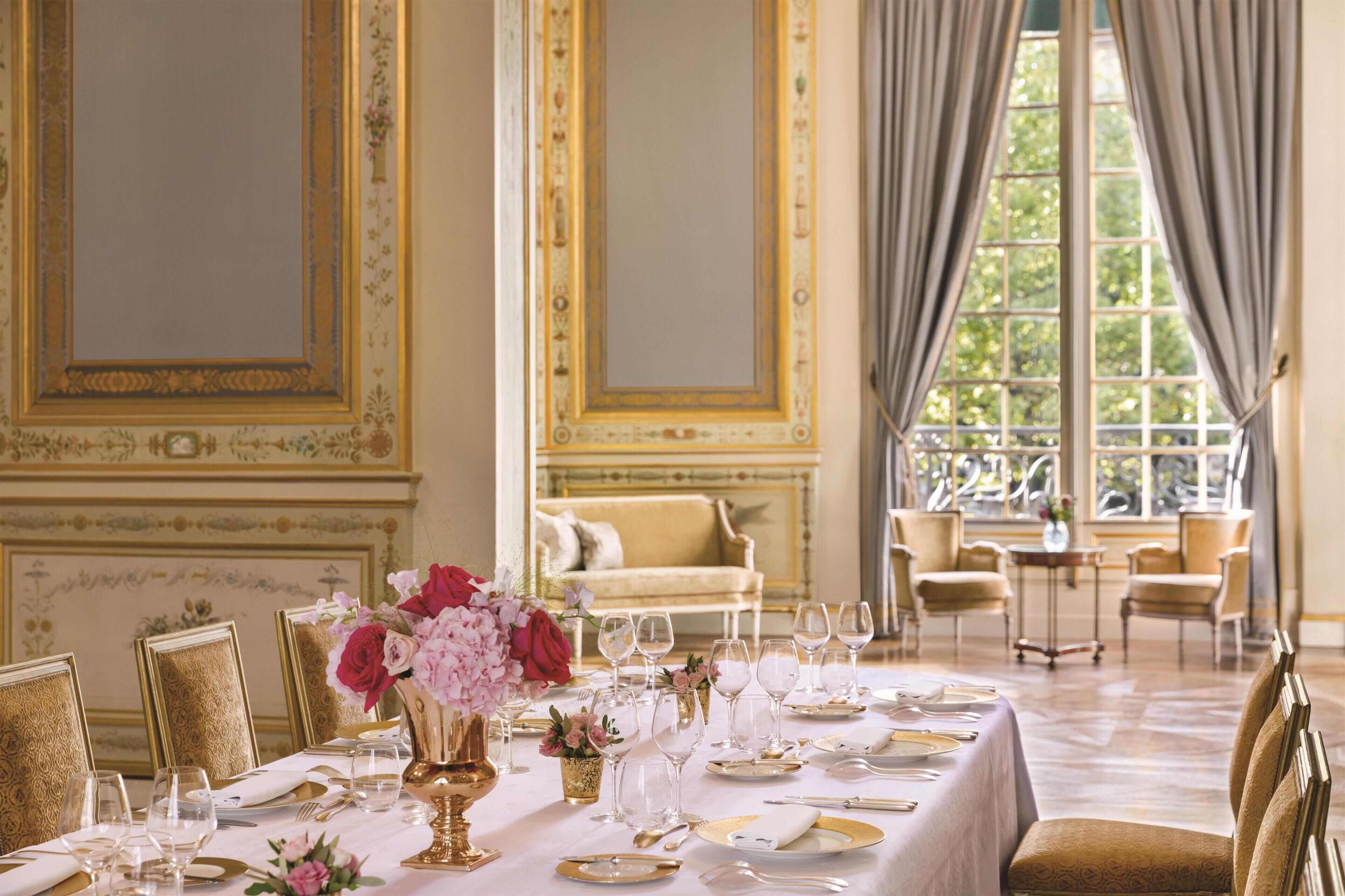 Un comedor formal con una mesa dispuesta para una comida, sillas y un sofá al fondo.
