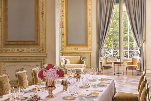 A formal dining room with a table set for a meal, chairs, and a sofa in the background.