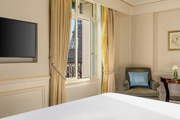 A hotel room with a bed, a chair, a small table with a vase, and a window with curtains. - Shangri-La Paris (Paris)