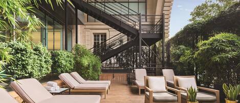 A rooftop lounge with lounge chairs, a staircase, and potted plants.