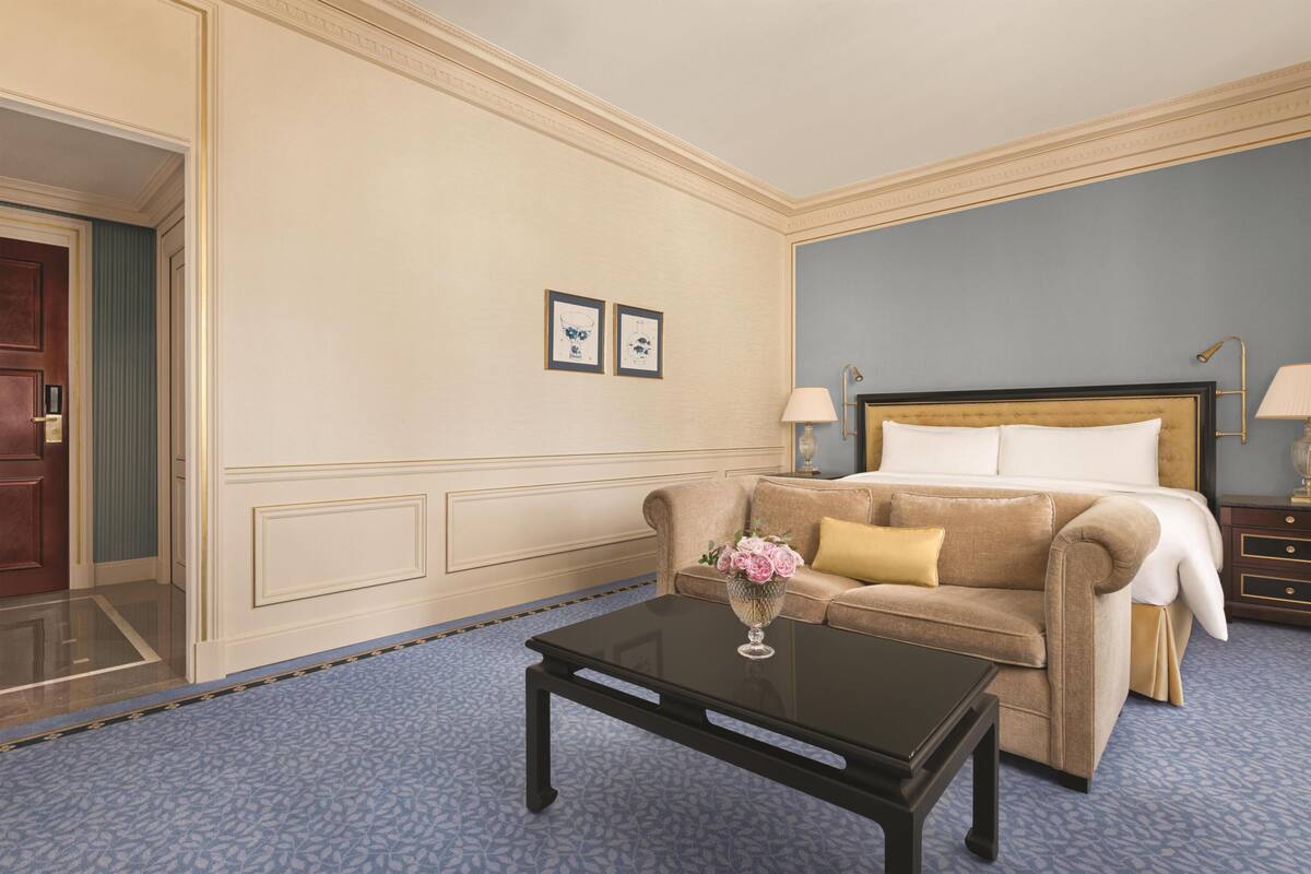 Une chambre d’hôtel avec un lit, un canapé, une table basse avec un vase et une porte.