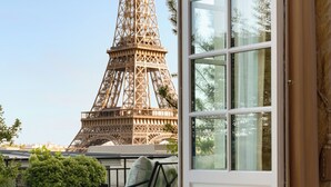 Un balcon avec vue sur la Tour Eiffel, une chaise, une table avec une bouteille de champagne et une fenêtre avec des rideaux.