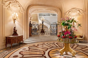 Een statige lobby met versierde decoratie, een trap en een bloemstuk.