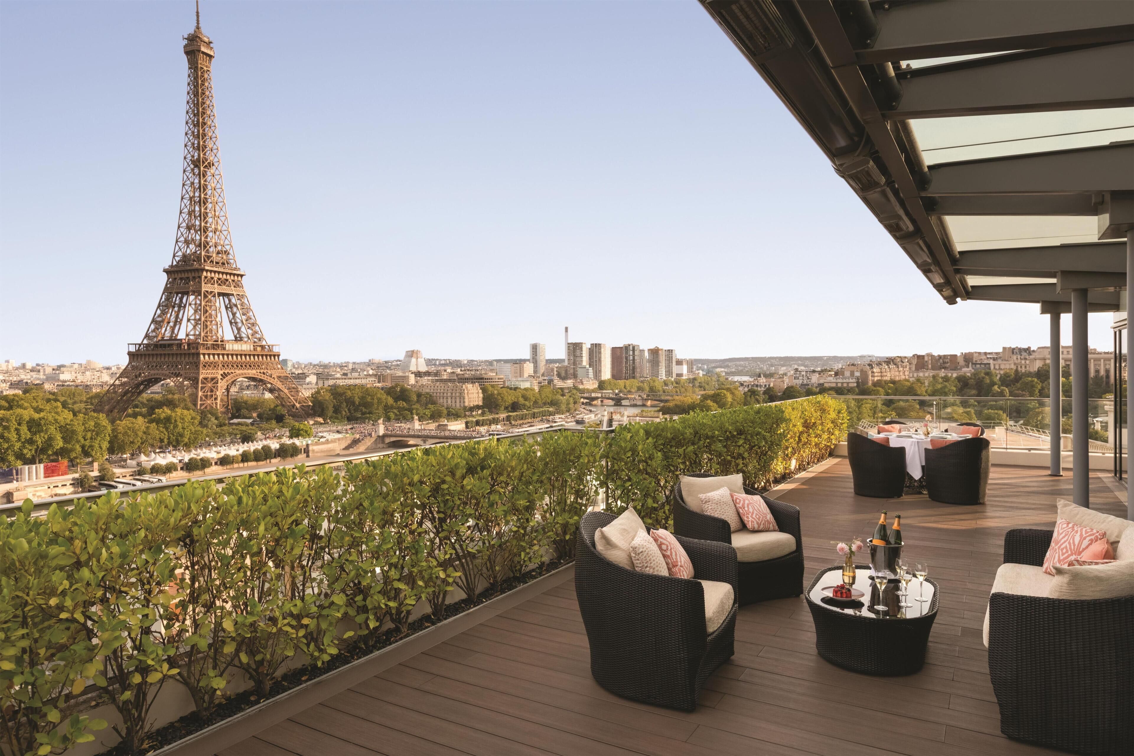 Una terraza en la azotea con mobiliario de mimbre, vistas a la Torre Eiffel y un paisaje urbano de fondo.
