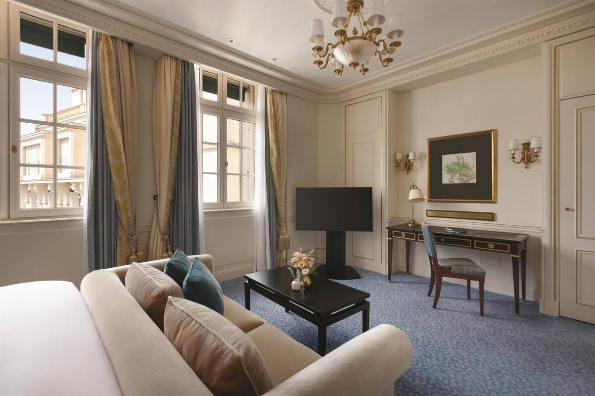 Une chambre d’hôtel comprenant un lit, un canapé, un bureau, une télévision et un lustre.