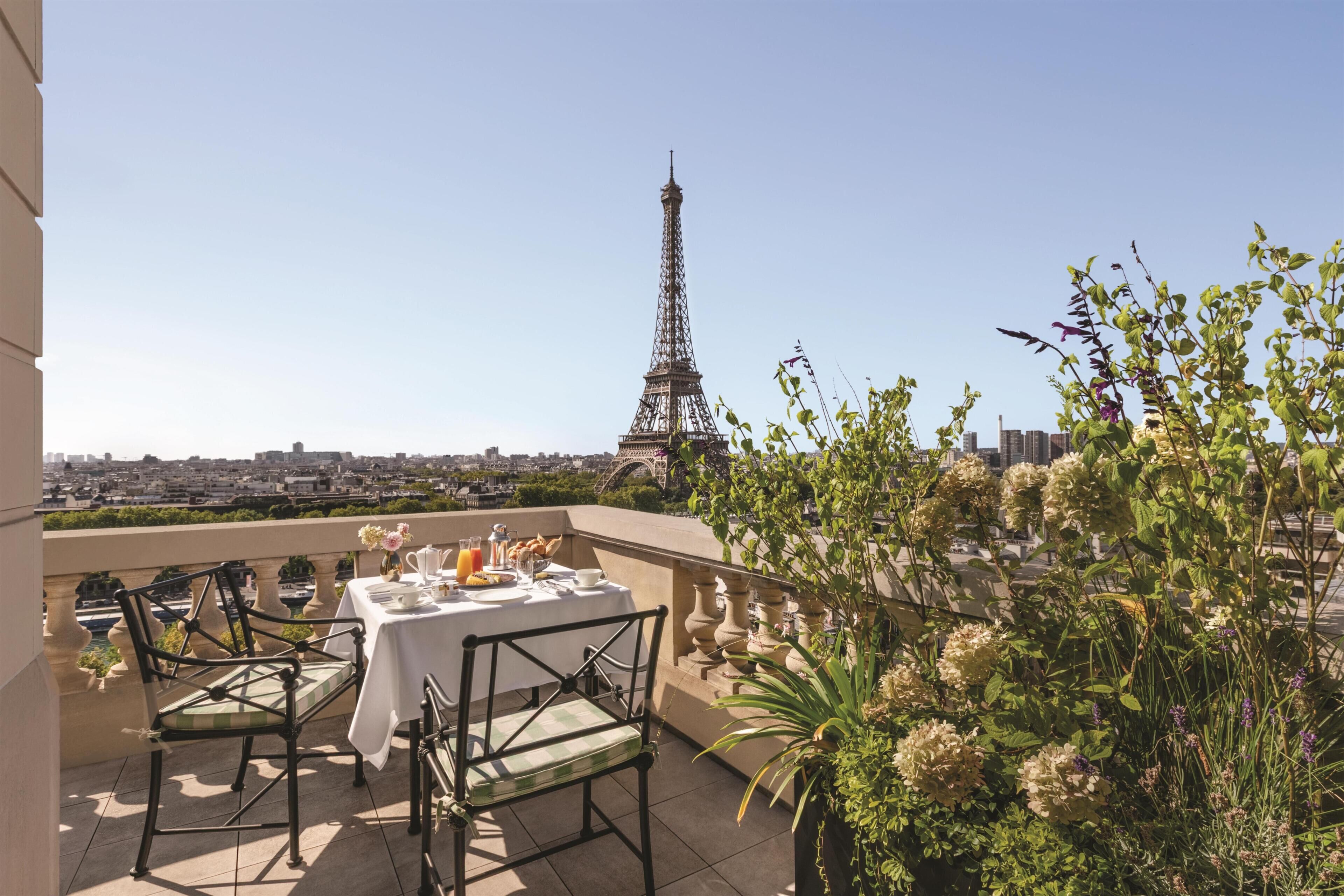 A balcony with a table set for two, chairs, and a view of the Eiffel Tower.