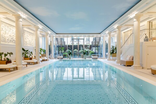 A large indoor swimming pool with a patterned floor, surrounded by columns and seating areas.