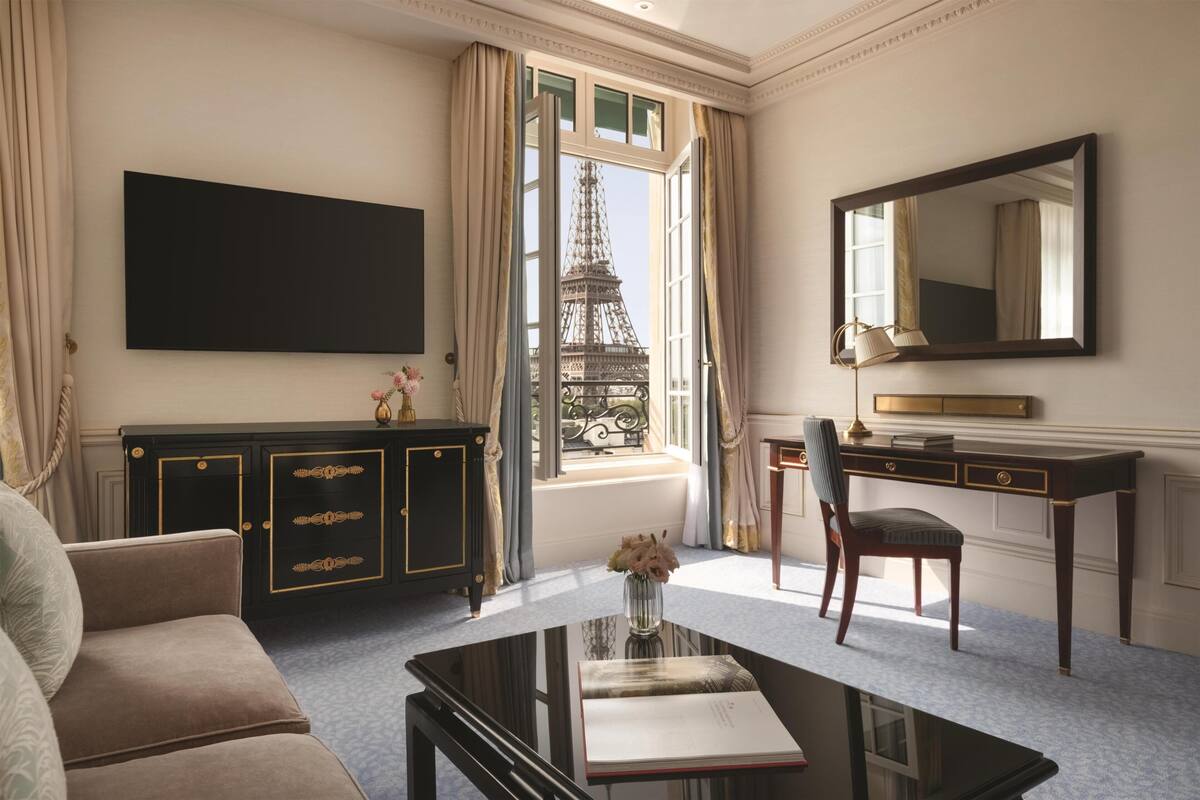Une pièce avec une grande fenêtre, un bureau noir, une chaise, un canapé et un téléviseur à écran plat.