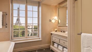 Un baño con un ventanal grande, una bañera, un tocador con espejo y vistas a la Torre Eiffel.