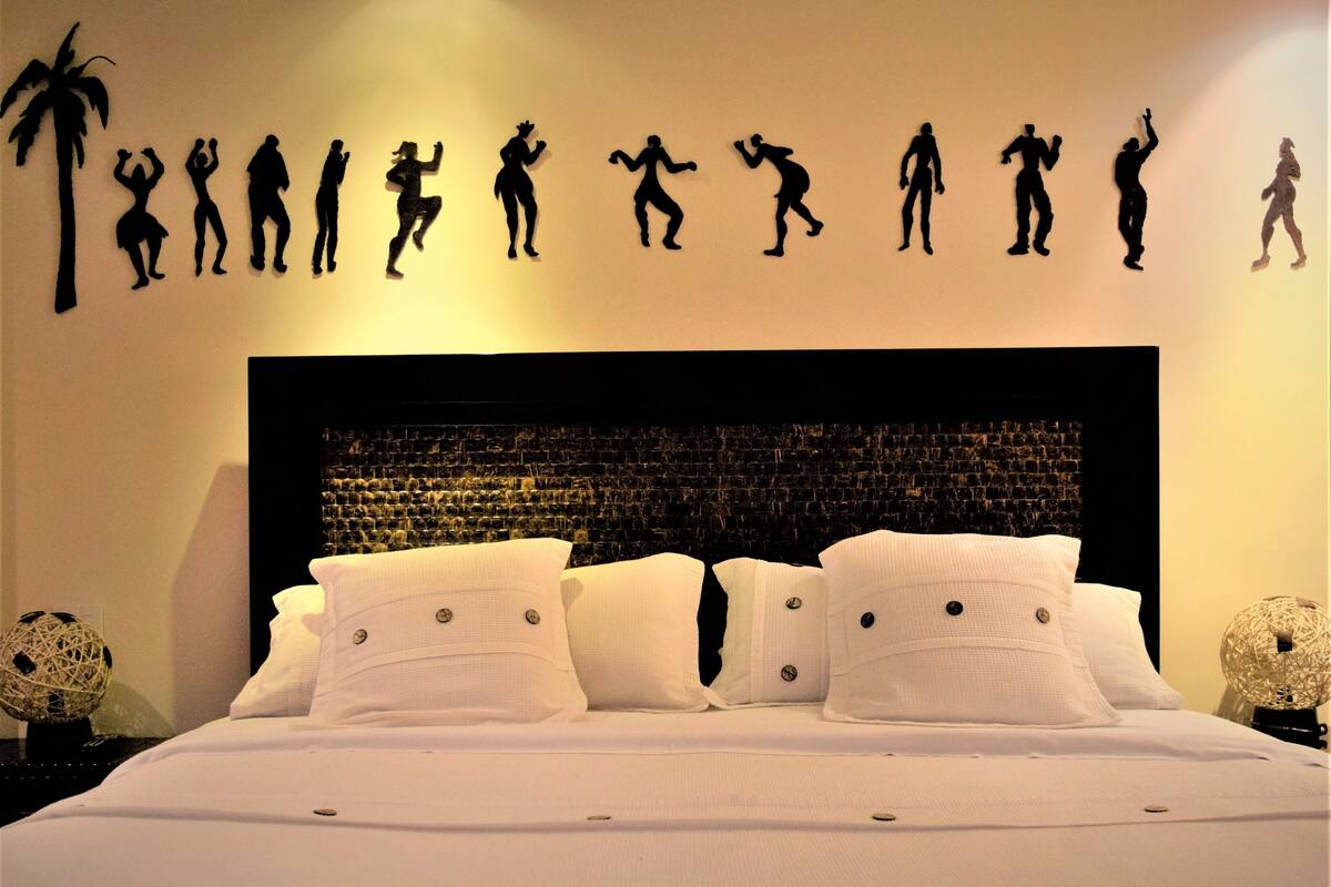 A hotel room with a large bed, white bedding, a textured headboard, and wall art depicting silhouetted figures in various poses.