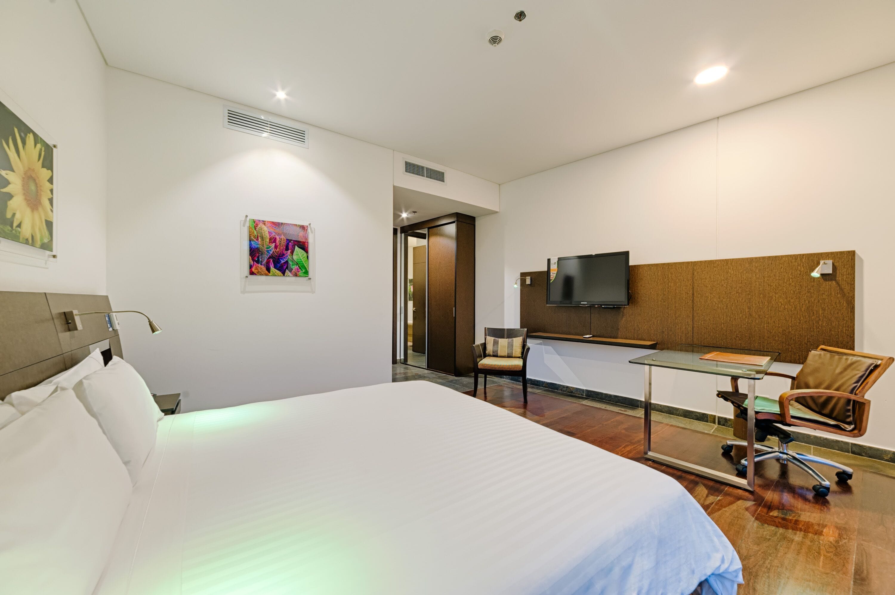 A hotel room with a large bed, a desk with a chair, a television, and artwork on the walls.