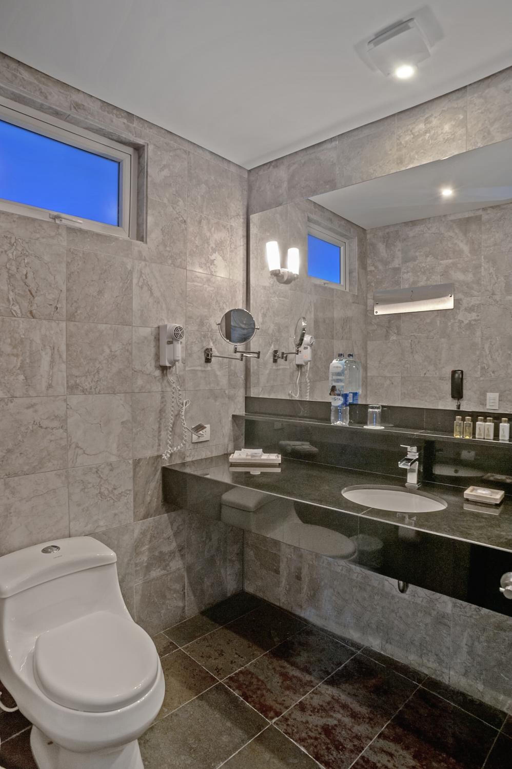 Un baño moderno con pared de mármol, un espejo grande, un inodoro y un lavabo.