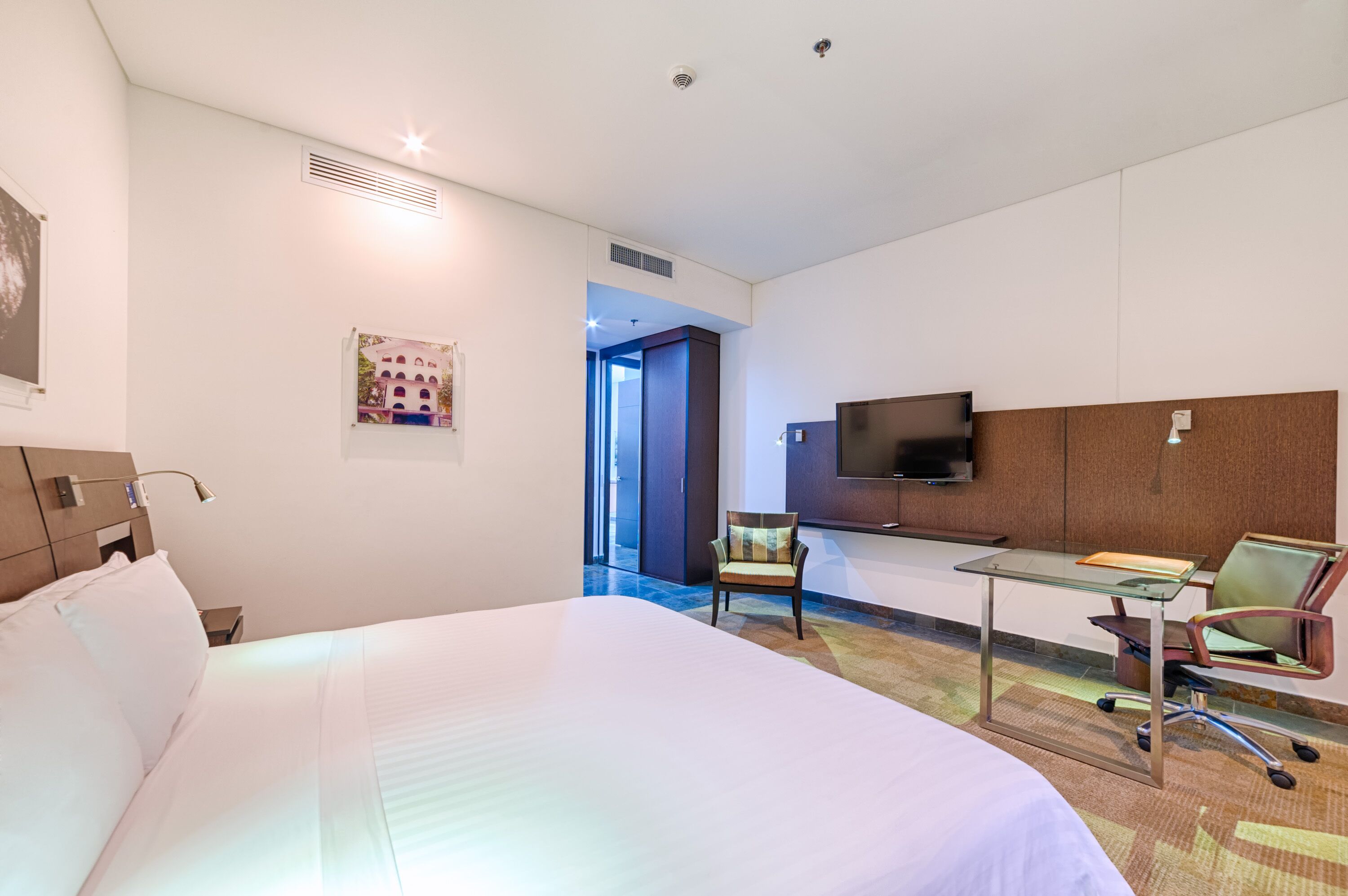 A hotel room with a large bed, a desk with a chair, a television, and a picture on the wall.