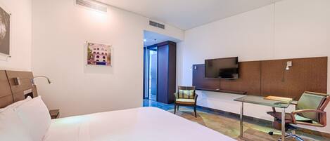 A hotel room with a large bed, a desk with a chair, a television, and a picture on the wall.