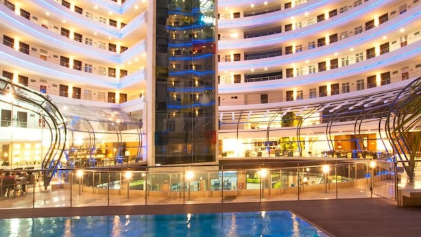 A multi-story hotel with a central atrium, a swimming pool, and a glass facade.