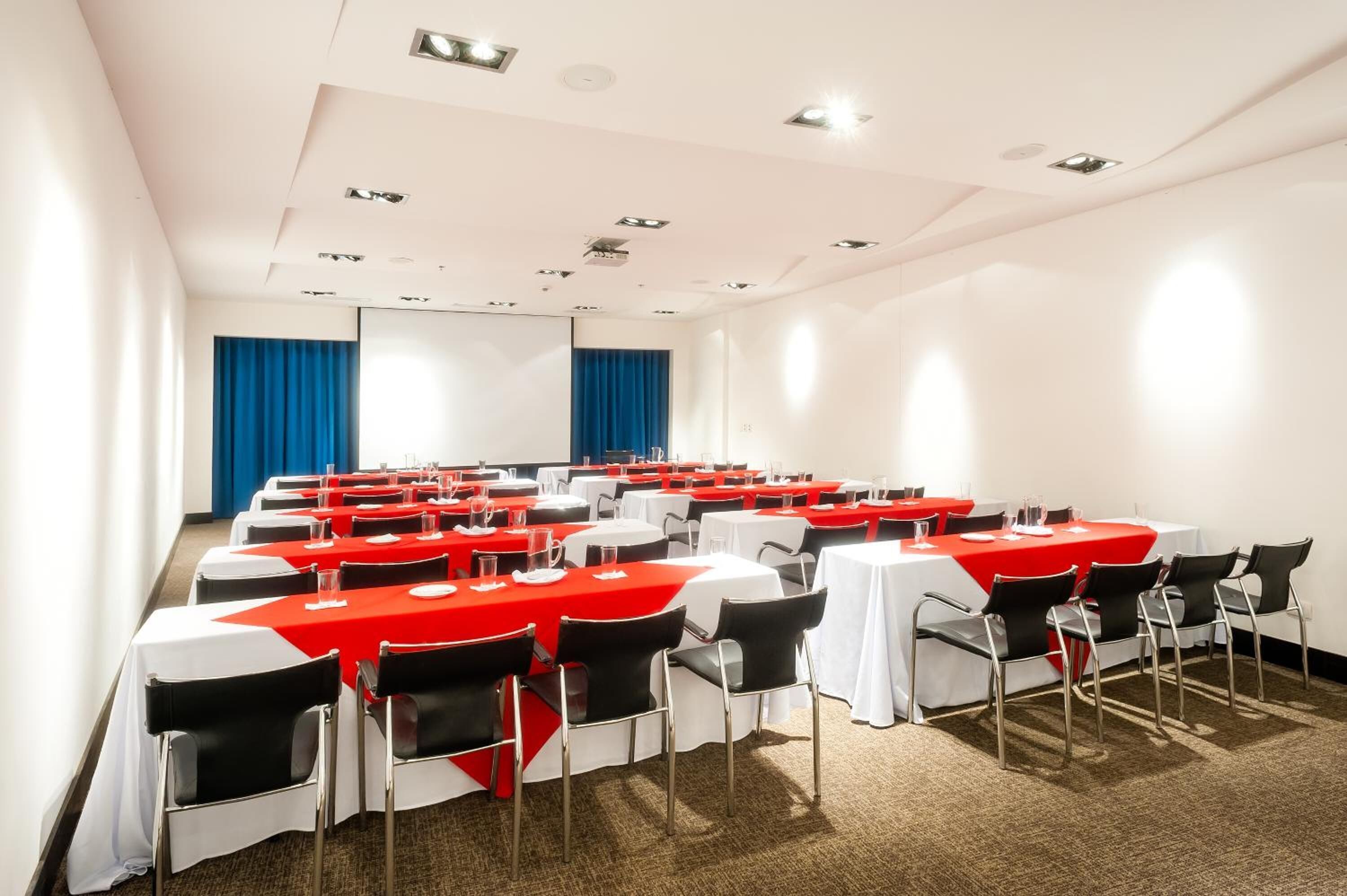 A conference room with rows of tables, each with a red tablecloth and black chairs.