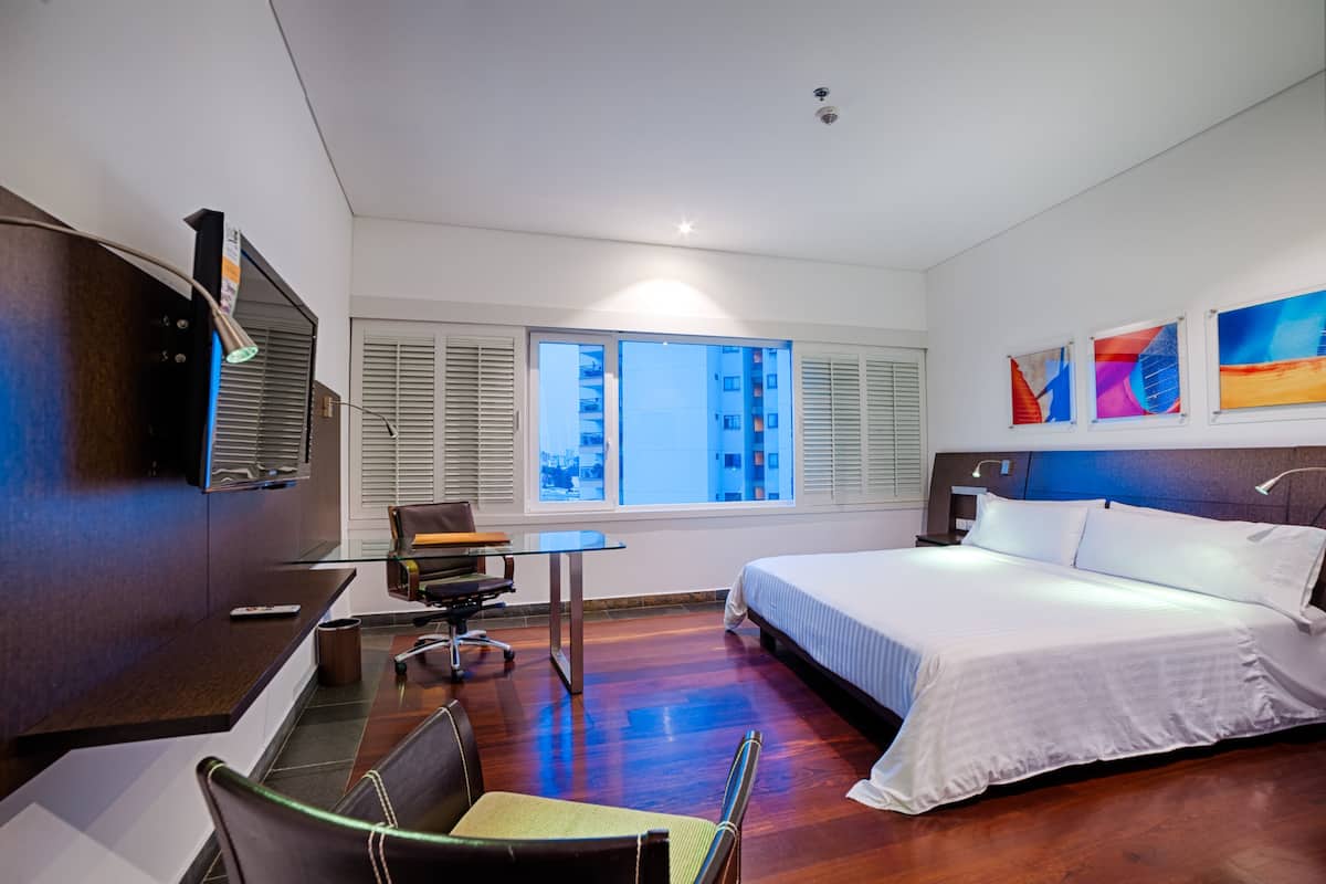 A hotel room with a bed, desk, chair, and a TV on the wall.