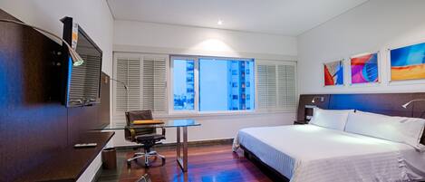 A hotel room with a bed, desk, chair, and a TV on the wall.