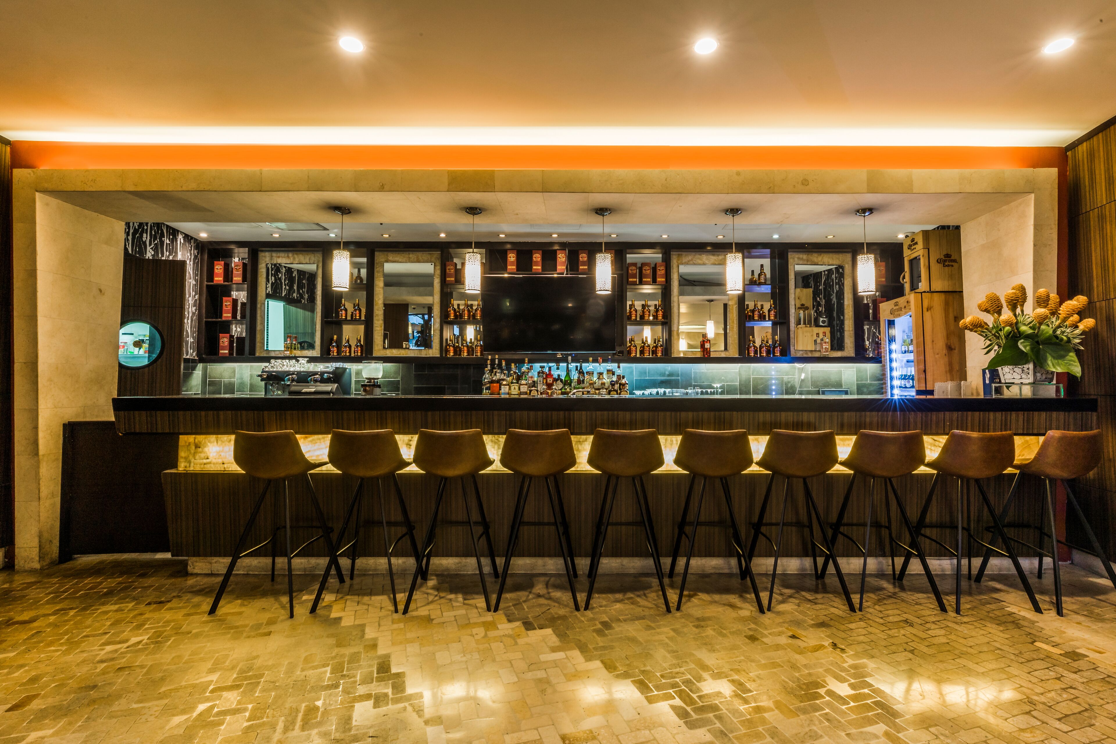 A bar area with a long counter, multiple stools, and a television screen.