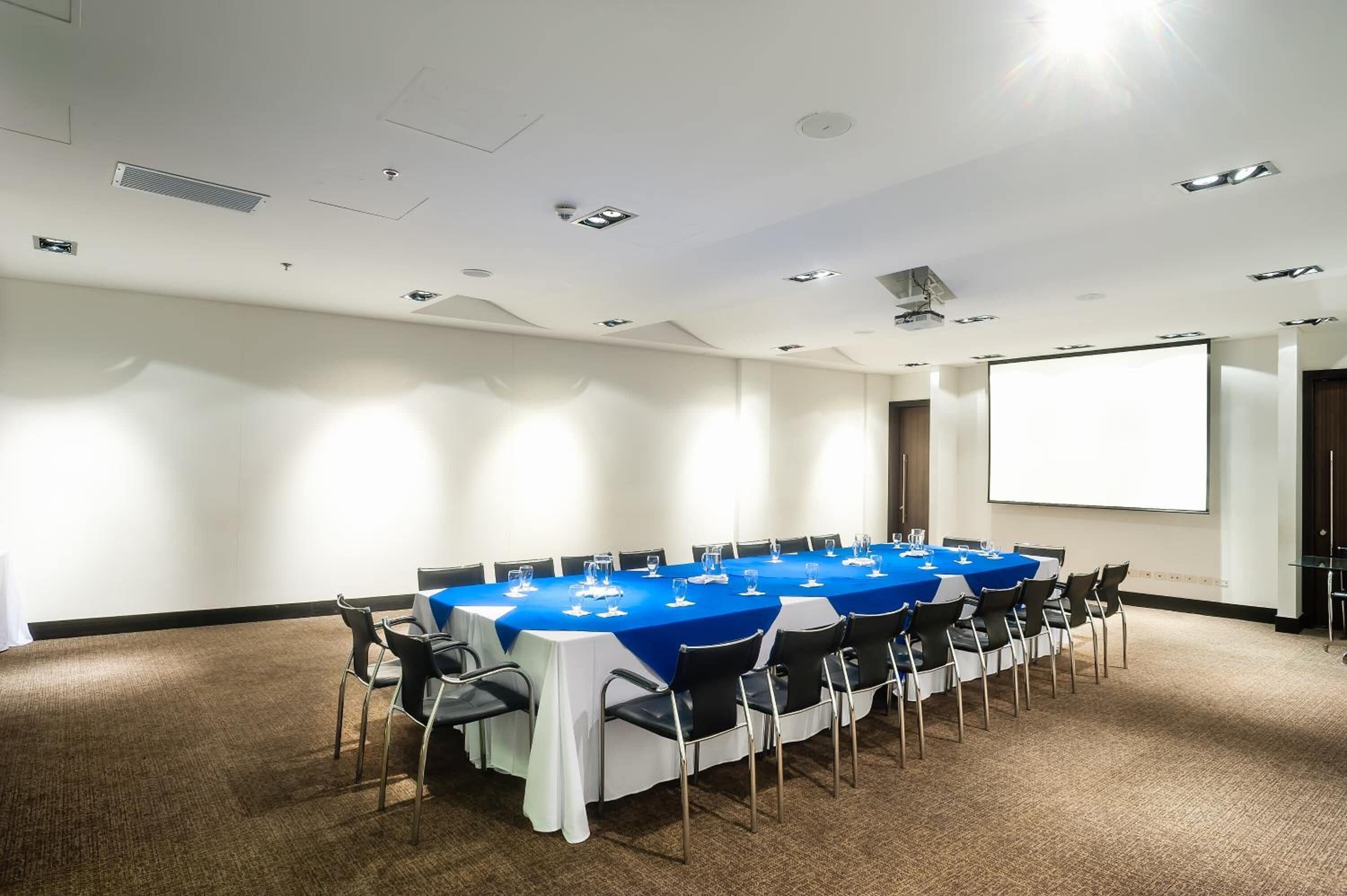 A conference room with a long table, chairs, a projector screen, and a carpeted floor.