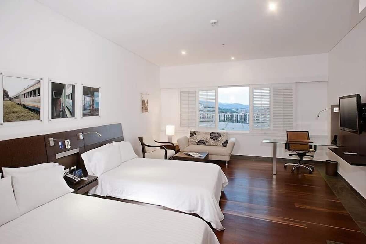 A hotel room with two beds, a sofa, a desk, a TV, and a window with a city view.