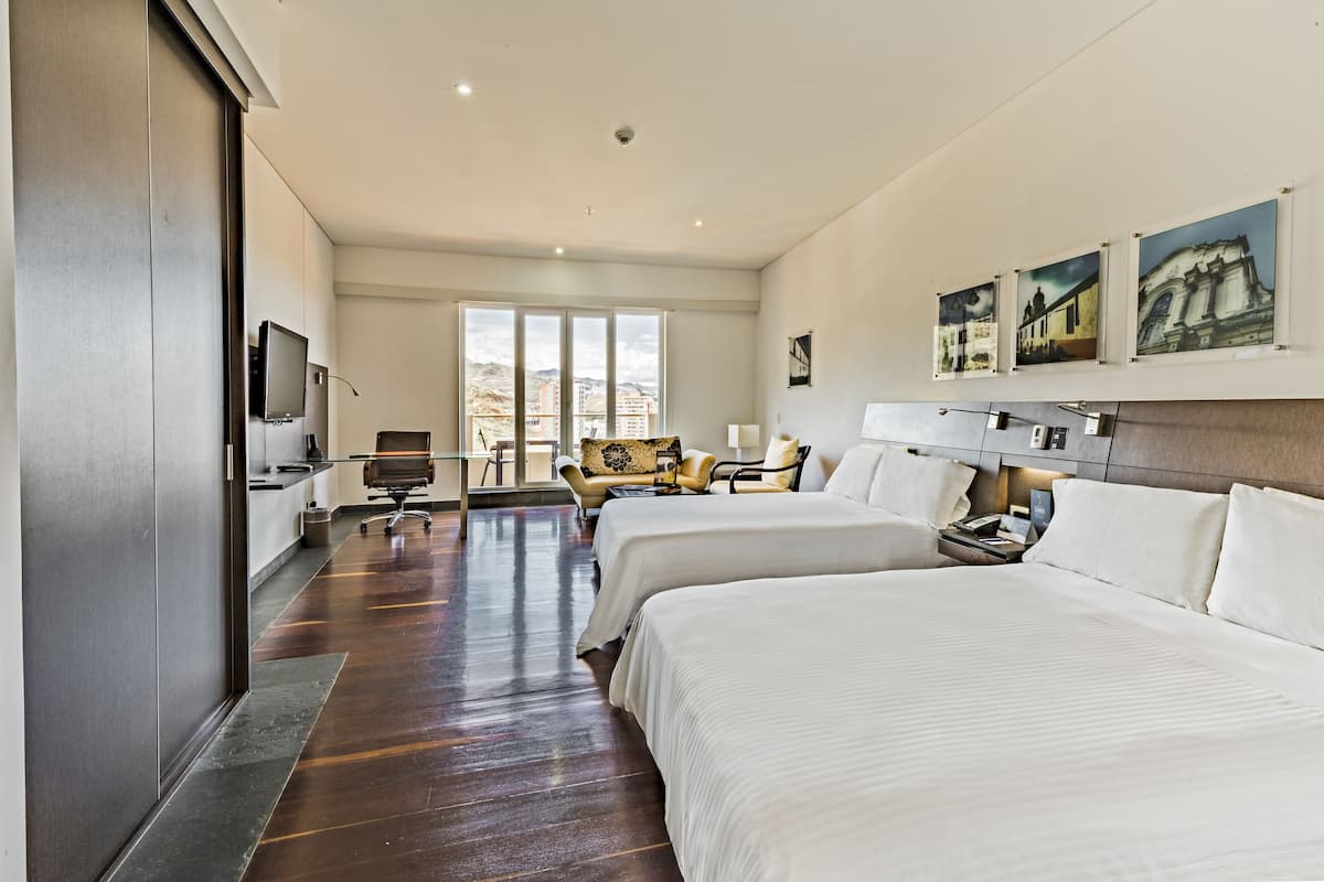 A hotel room with two beds, a desk, a chair, and a television.