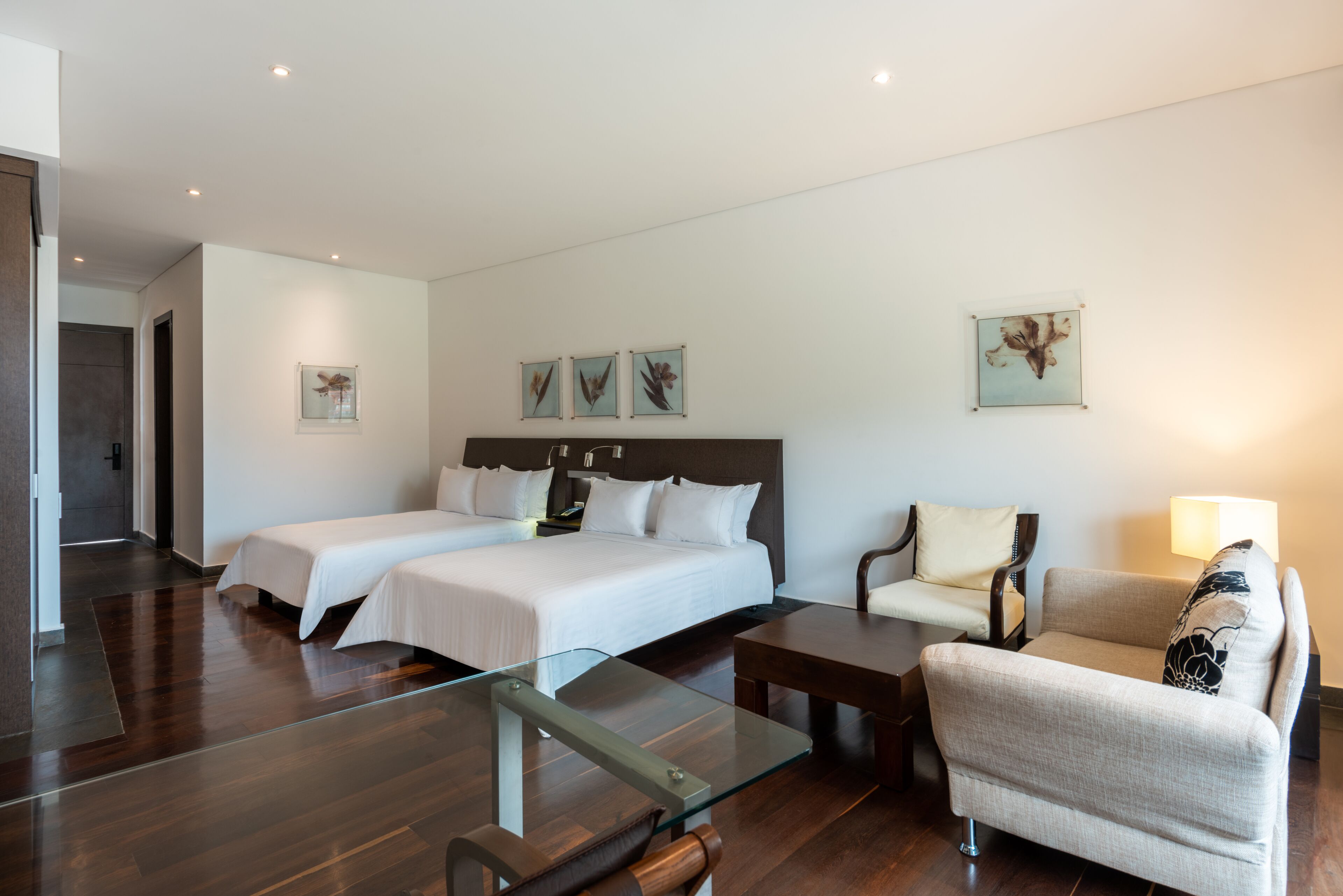 A hotel room with two beds, a glass coffee table, a sofa, and a chair.