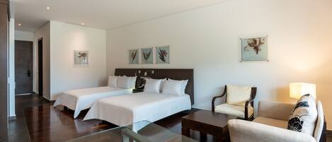 A hotel room with two beds, a glass coffee table, a sofa, and a chair.