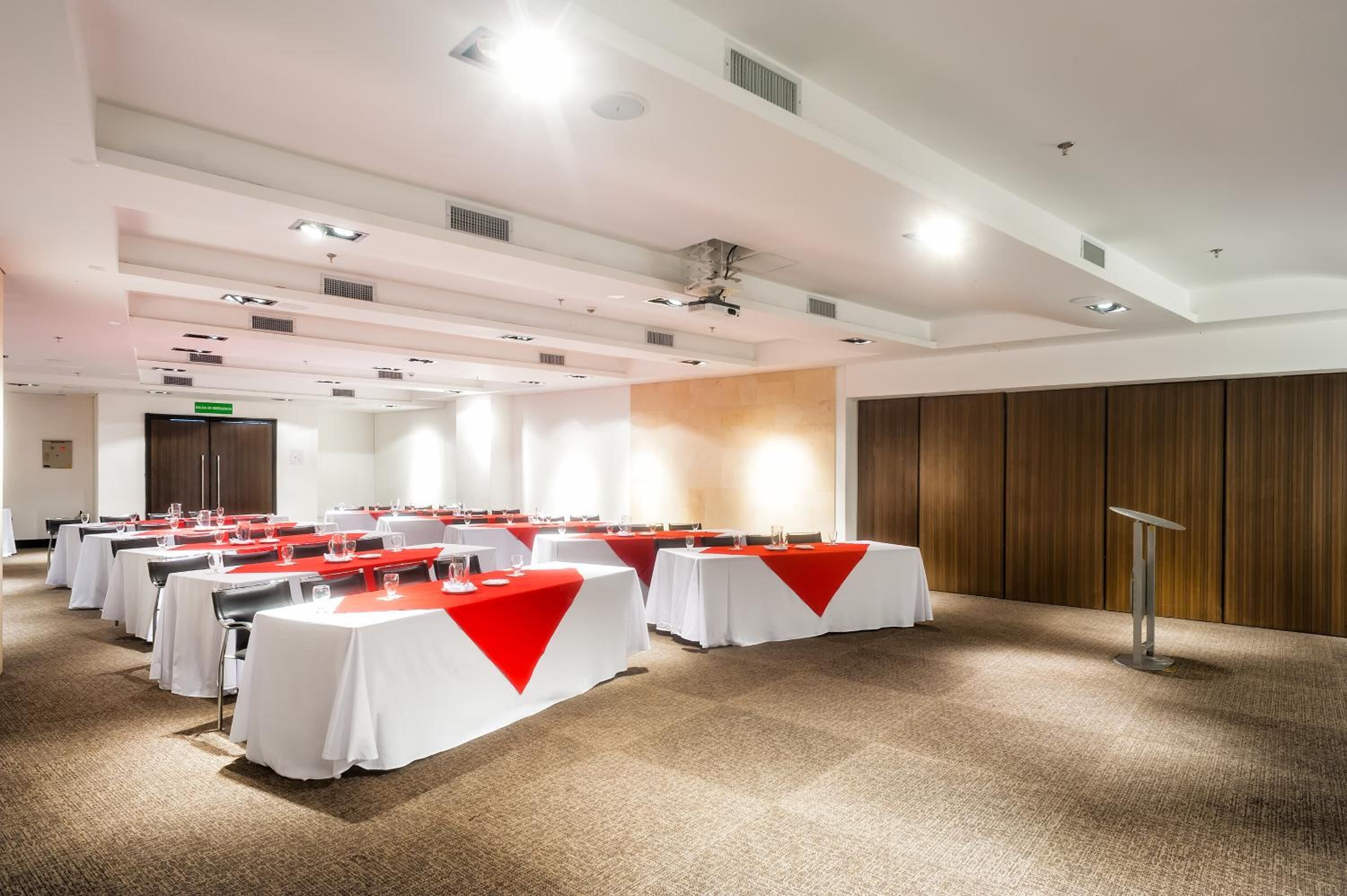 A conference room with multiple tables, each covered with a white tablecloth and red runners, arranged in rows.