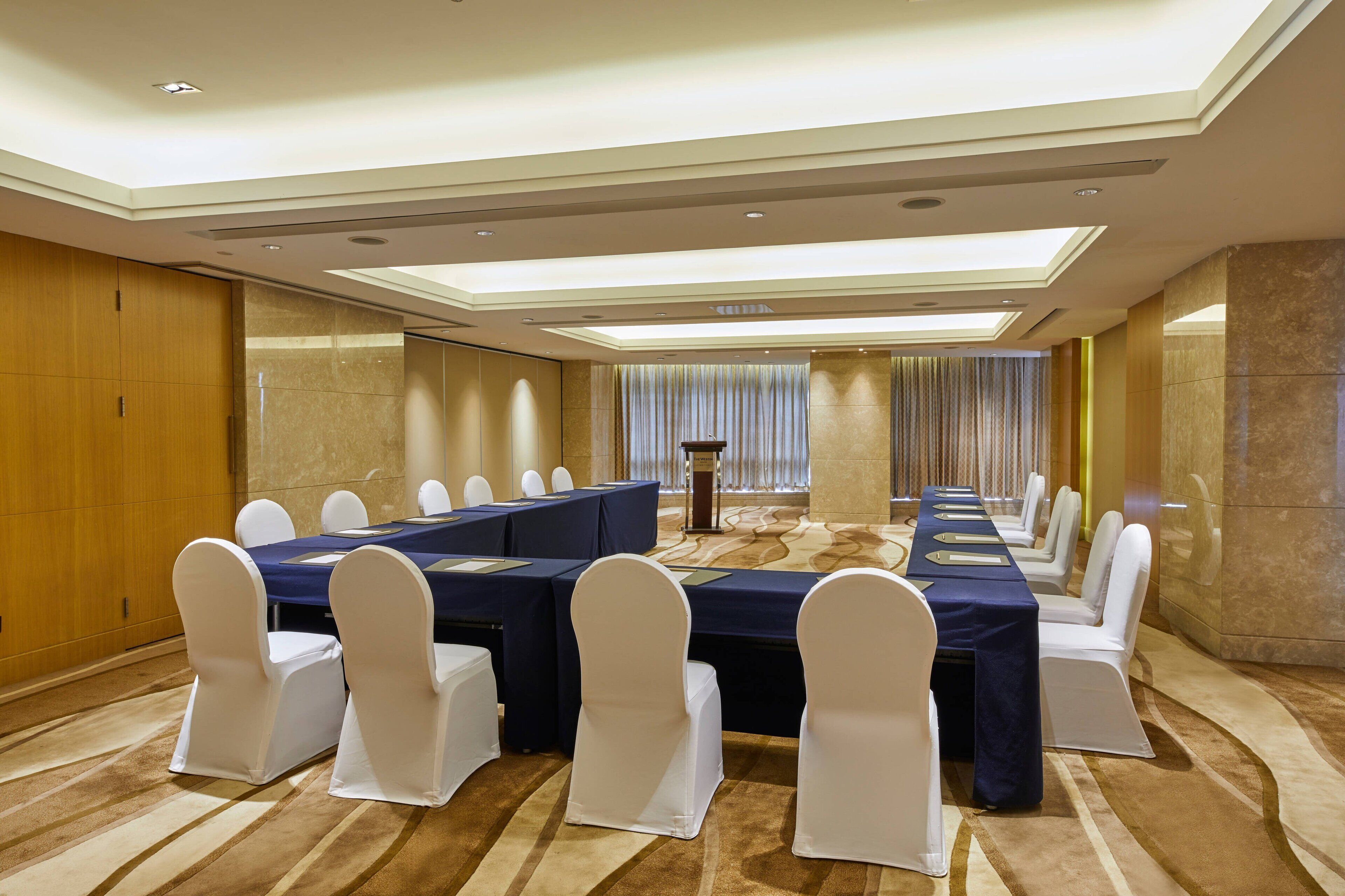 A conference room with a long table, white chairs, and a carpeted floor.