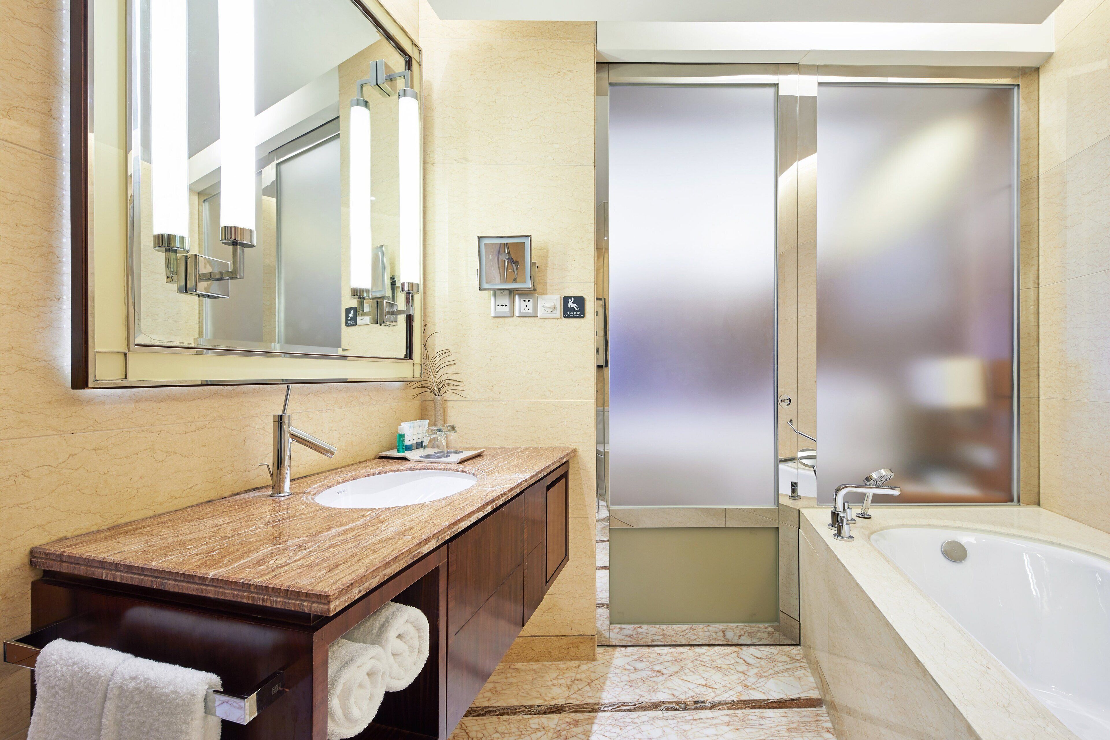 Un baño moderno con lavamanos de mármol, un espejo grande, una bañera y una puerta de ducha con vidrio esmerilado.