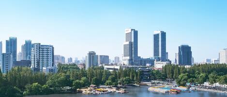 A cityscape with modern high-rise buildings, a river with boats, and a park area with trees.