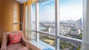 Una habitación con un amplio ventanal, un sillón mullido y vistas a un paisaje urbano.