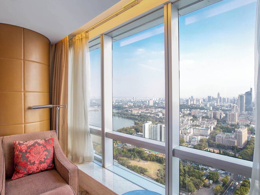 A room with a large window, a cushioned chair, and a view of a cityscape.