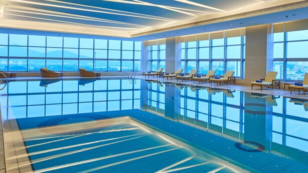 Una piscina interior con agua cristalina, ventanas amplias y tumbonas.